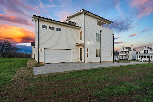 back house at dusk with a lawn, a garage, and a patio