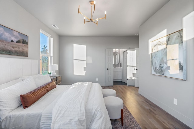 bedroom with ensuite bath, dark wood-type flooring, and a chandelier