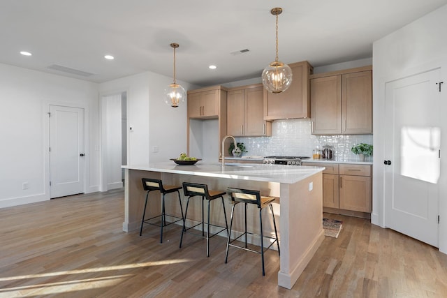 kitchen featuring light hardwood / wood-style flooring, pendant lighting, a kitchen island with sink, backsplash, and stove