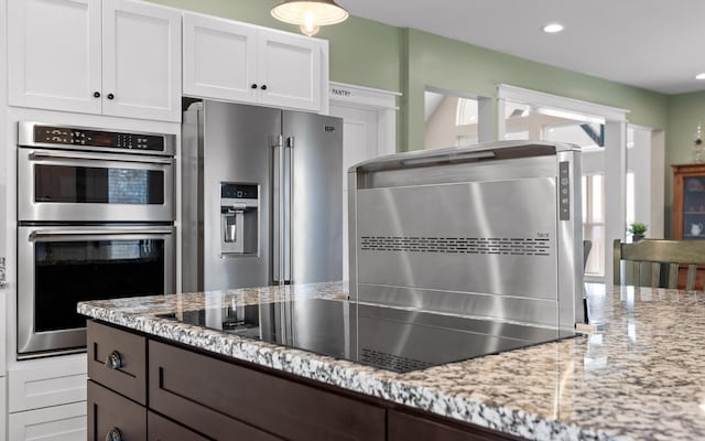 kitchen with stainless steel appliances, white cabinetry, and light stone counters