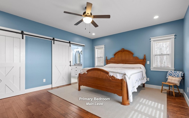 bedroom with dark hardwood / wood-style flooring, a barn door, ensuite bathroom, and ceiling fan