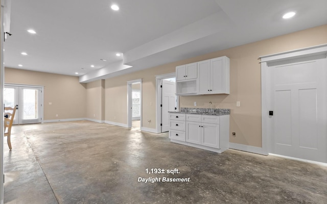 kitchen featuring light stone counters, french doors, white cabinets, and concrete flooring