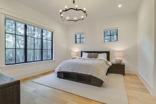 bedroom with a chandelier, light wood-type flooring, and multiple windows