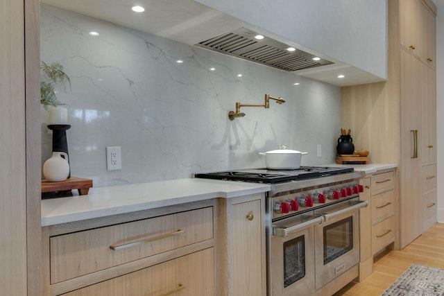 kitchen featuring range with two ovens, light brown cabinetry, light wood-type flooring, and extractor fan