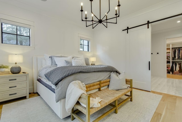 bedroom featuring an inviting chandelier, a walk in closet, a barn door, light hardwood / wood-style floors, and a closet