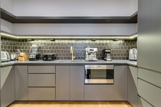 kitchen with decorative backsplash, gray cabinets, sink, and light hardwood / wood-style flooring