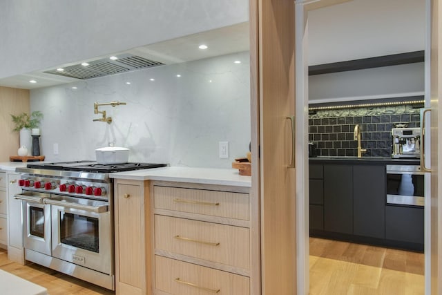 kitchen with decorative backsplash, light brown cabinets, light hardwood / wood-style flooring, and range with two ovens