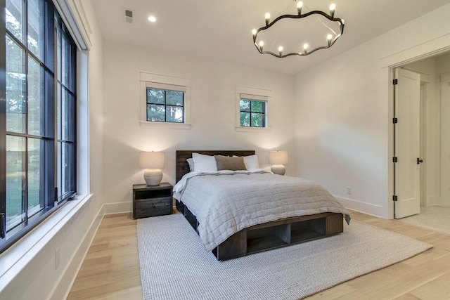 bedroom featuring light hardwood / wood-style flooring, multiple windows, and a notable chandelier