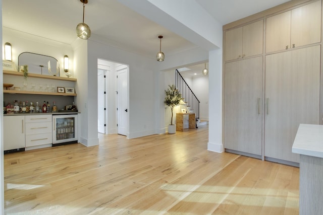 interior space featuring decorative light fixtures, crown molding, beverage cooler, and light hardwood / wood-style flooring