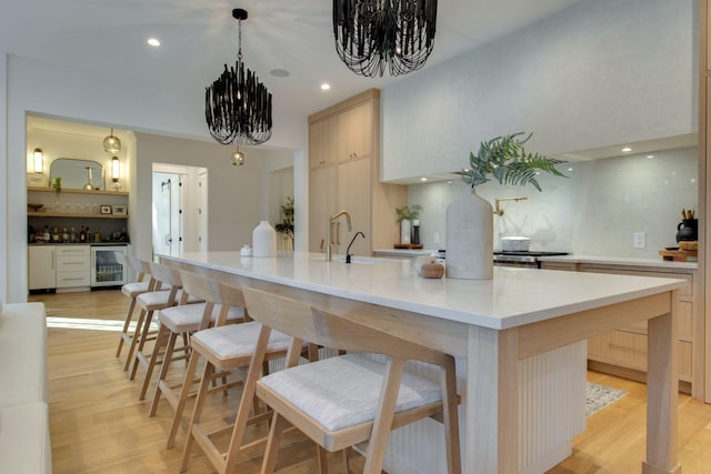 kitchen featuring sink, light hardwood / wood-style flooring, an island with sink, beverage cooler, and a chandelier