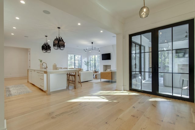 interior space with white cabinets, light wood-type flooring, a kitchen island with sink, and hanging light fixtures