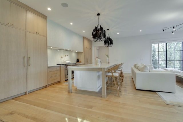 kitchen with electric stove, a kitchen island with sink, decorative light fixtures, and light wood-type flooring