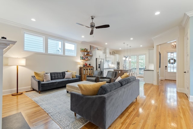 living room with ceiling fan with notable chandelier, light hardwood / wood-style floors, crown molding, and sink