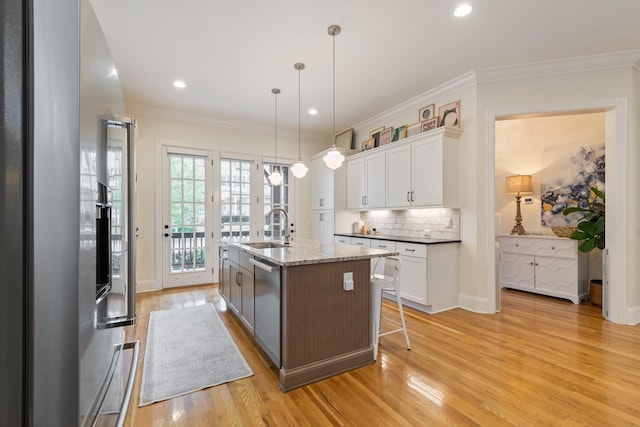 kitchen featuring white cabinetry, an island with sink, light wood-type flooring, decorative light fixtures, and appliances with stainless steel finishes