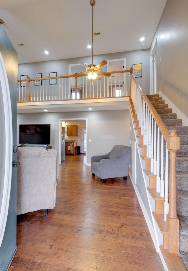 unfurnished living room with hardwood / wood-style floors, ceiling fan, and a high ceiling