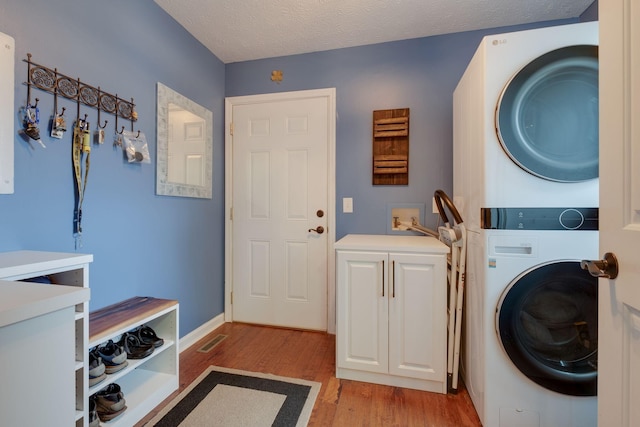 laundry area featuring cabinets, stacked washing maching and dryer, a textured ceiling, and light hardwood / wood-style flooring