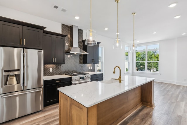 kitchen with sink, stainless steel appliances, a center island with sink, and wall chimney range hood