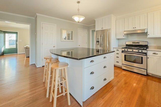 kitchen featuring appliances with stainless steel finishes, decorative light fixtures, white cabinetry, ornamental molding, and a center island