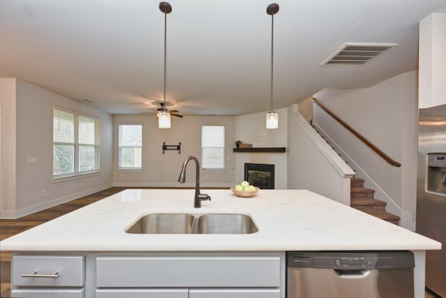 kitchen featuring sink, stainless steel appliances, an island with sink, pendant lighting, and a fireplace