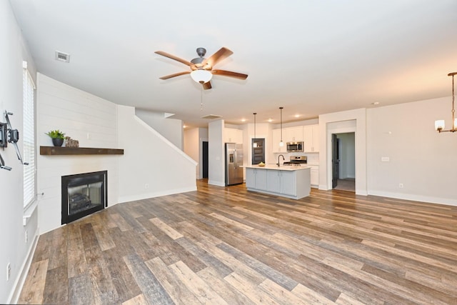 unfurnished living room featuring wood-type flooring, ceiling fan with notable chandelier, and sink