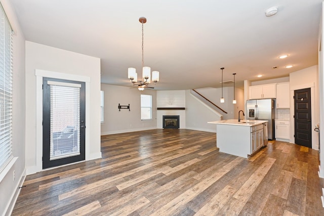 kitchen with pendant lighting, hardwood / wood-style floors, stainless steel refrigerator with ice dispenser, an island with sink, and white cabinetry