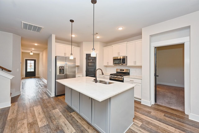 kitchen with a kitchen island with sink, white cabinets, sink, dark hardwood / wood-style flooring, and stainless steel appliances