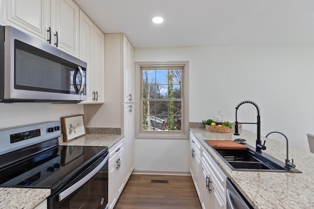 kitchen with sink, dark hardwood / wood-style floors, light stone counters, white cabinetry, and stainless steel appliances