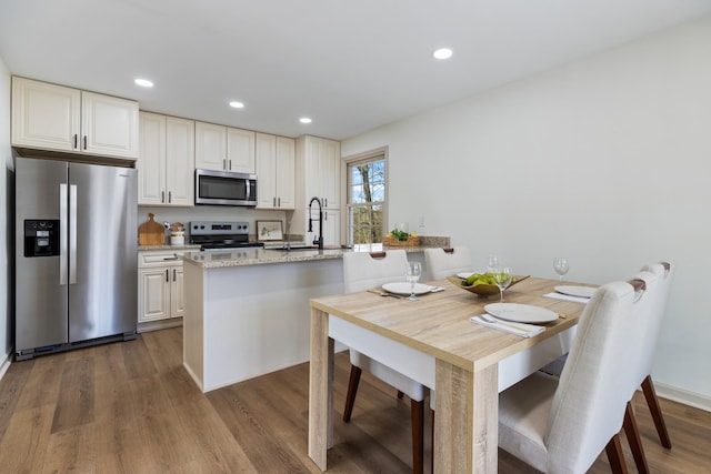 kitchen with a kitchen island with sink, sink, light stone countertops, dark hardwood / wood-style flooring, and stainless steel appliances