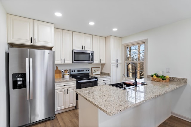 kitchen with kitchen peninsula, appliances with stainless steel finishes, sink, wood-type flooring, and white cabinetry