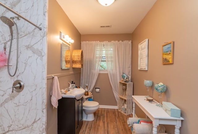 bathroom with hardwood / wood-style flooring, vanity, toilet, and tiled shower