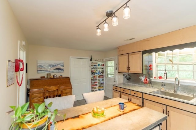 kitchen featuring light brown cabinetry, backsplash, light stone counters, and sink