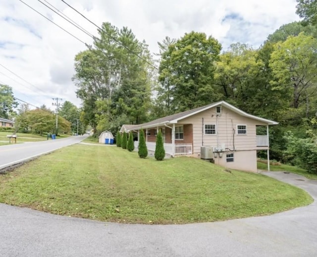 view of front of home with a shed, covered porch, central AC unit, and a front yard