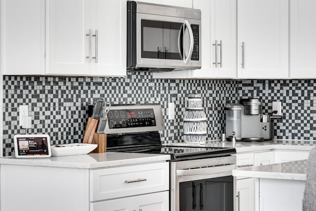 kitchen with tasteful backsplash, white cabinets, and appliances with stainless steel finishes