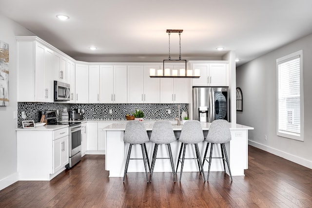 kitchen featuring white cabinetry, stainless steel appliances, dark hardwood / wood-style flooring, pendant lighting, and a center island with sink