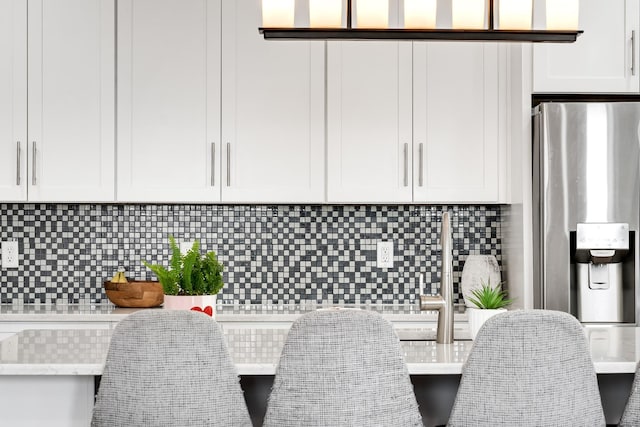 kitchen with white cabinets, decorative backsplash, light stone countertops, and stainless steel fridge with ice dispenser