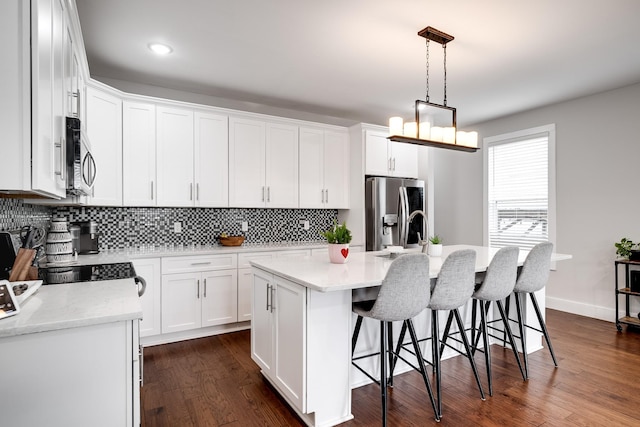 kitchen with appliances with stainless steel finishes, white cabinetry, a kitchen island with sink, and dark wood-type flooring