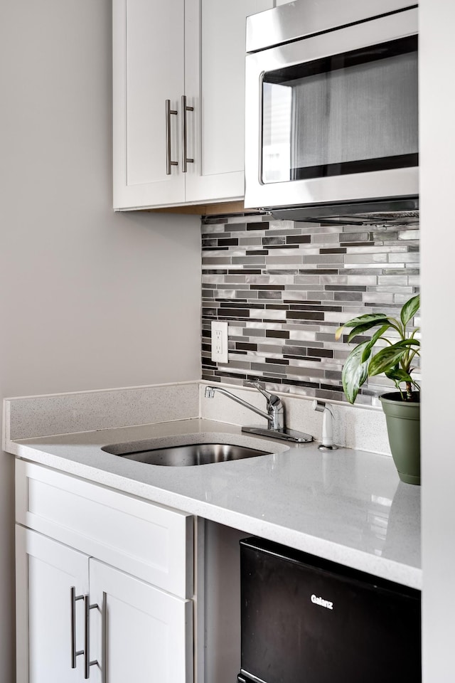 kitchen with backsplash, white cabinetry, and sink