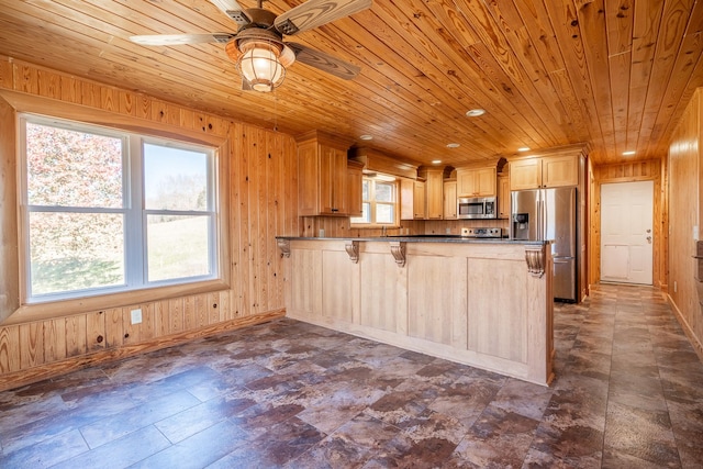 kitchen featuring a breakfast bar, light brown cabinetry, wooden walls, kitchen peninsula, and stainless steel appliances