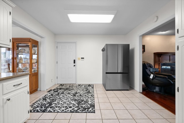 kitchen with stainless steel refrigerator, white cabinetry, and light tile patterned floors