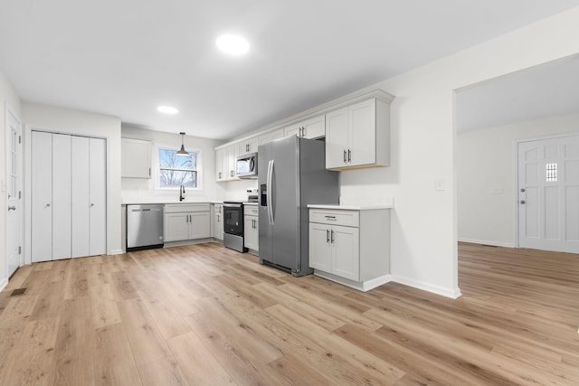 kitchen with white cabinetry, pendant lighting, stainless steel appliances, and light hardwood / wood-style floors