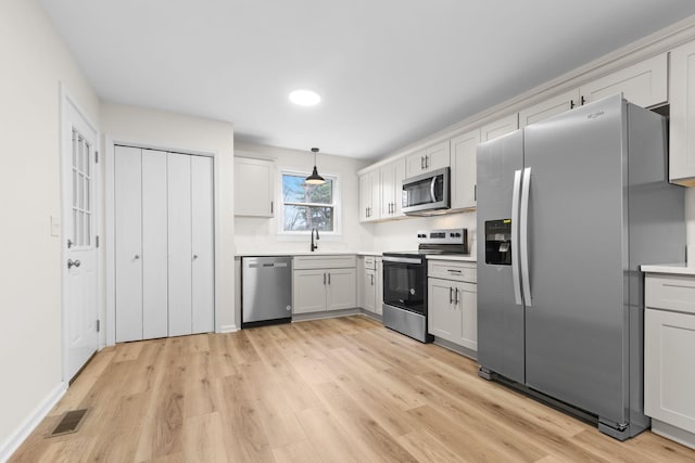 kitchen featuring white cabinetry, sink, hanging light fixtures, stainless steel appliances, and light wood-type flooring