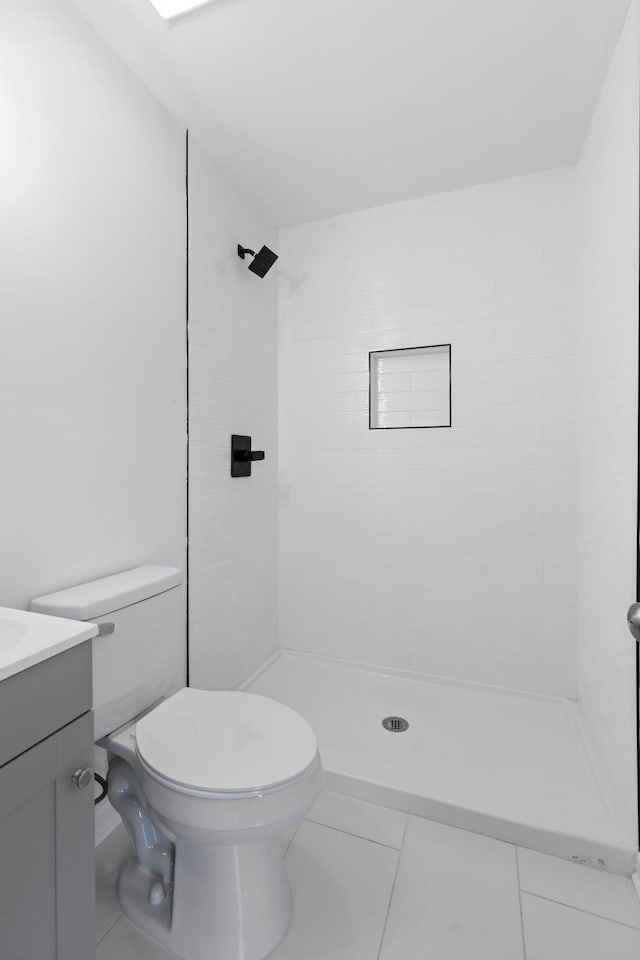 bathroom with tile patterned floors, vanity, a tile shower, and toilet