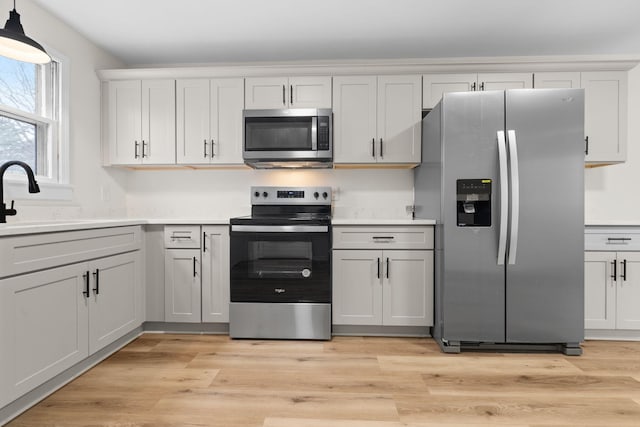 kitchen featuring light wood-type flooring, stainless steel appliances, sink, pendant lighting, and white cabinetry