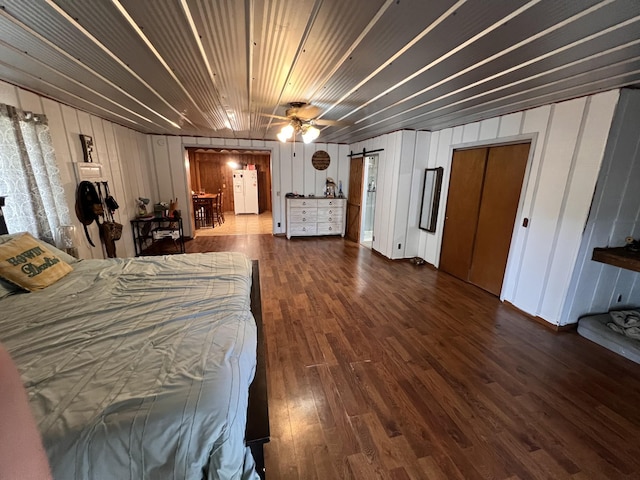 bedroom with dark hardwood / wood-style floors, white fridge with ice dispenser, wooden walls, and ceiling fan