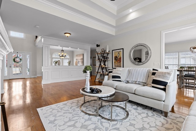 living room featuring ornate columns, hardwood / wood-style flooring, a tray ceiling, ornamental molding, and an inviting chandelier