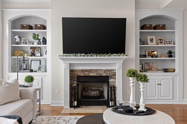 living room featuring light hardwood / wood-style floors, built in features, and a stone fireplace