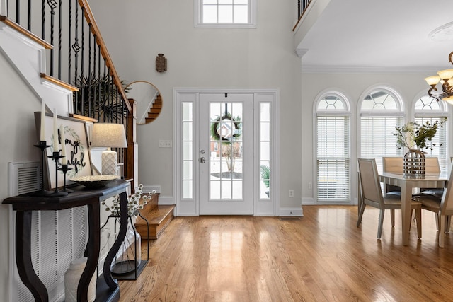 foyer entrance with light wood-type flooring, a high ceiling, an inviting chandelier, and ornamental molding