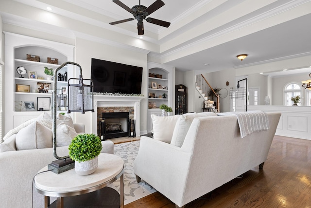 living room with crown molding, a fireplace, built in shelves, dark hardwood / wood-style flooring, and ceiling fan with notable chandelier