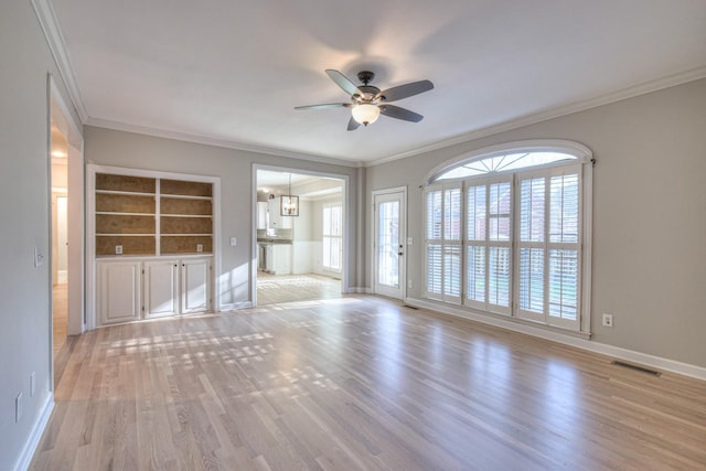 unfurnished living room with ceiling fan with notable chandelier, built in shelves, light wood-type flooring, and ornamental molding