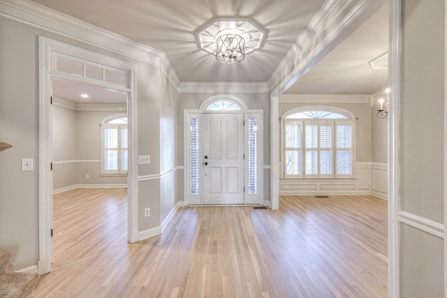 foyer entrance with crown molding, a notable chandelier, and light wood-type flooring